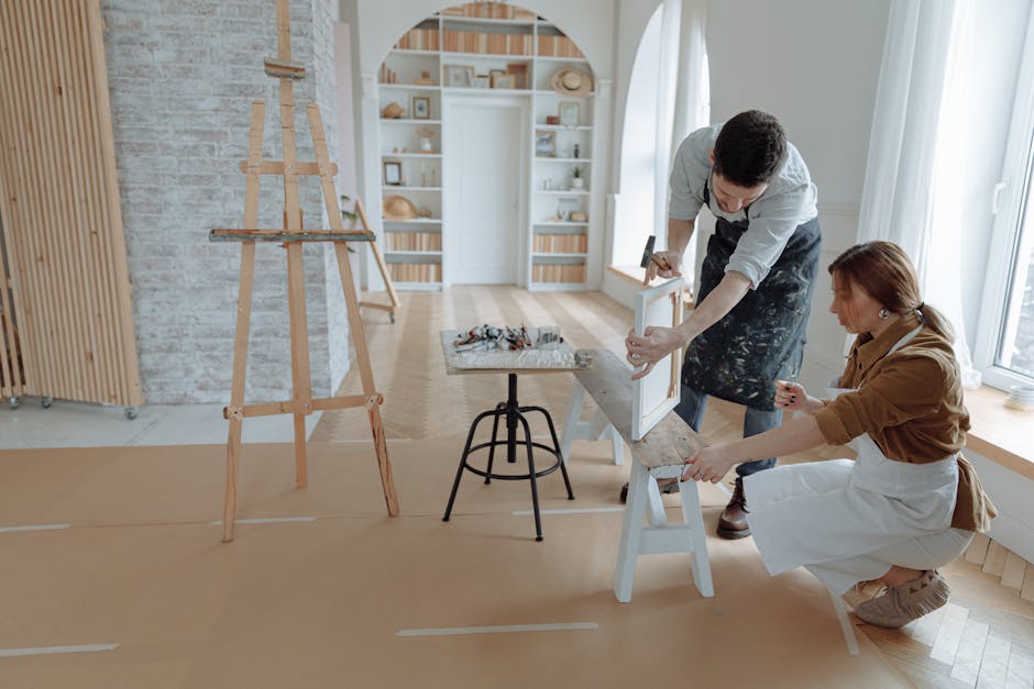 Man and woman working together in an art studio, preparing canvas on an easel.