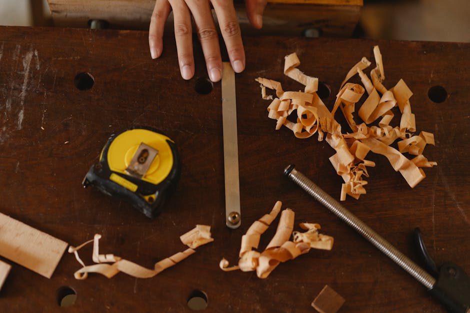 From above of crop anonymous woodworker with assorted instruments and wooden shavings in workshop